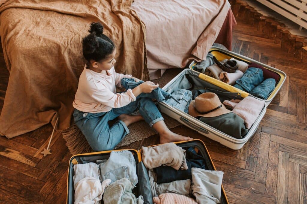 little girl packing suitcases while sitting on the floor