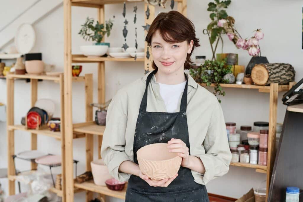 A young woman in an art studio business space holding a handcrafted bowl, representing self-employment and entrepreneurship in Alberta