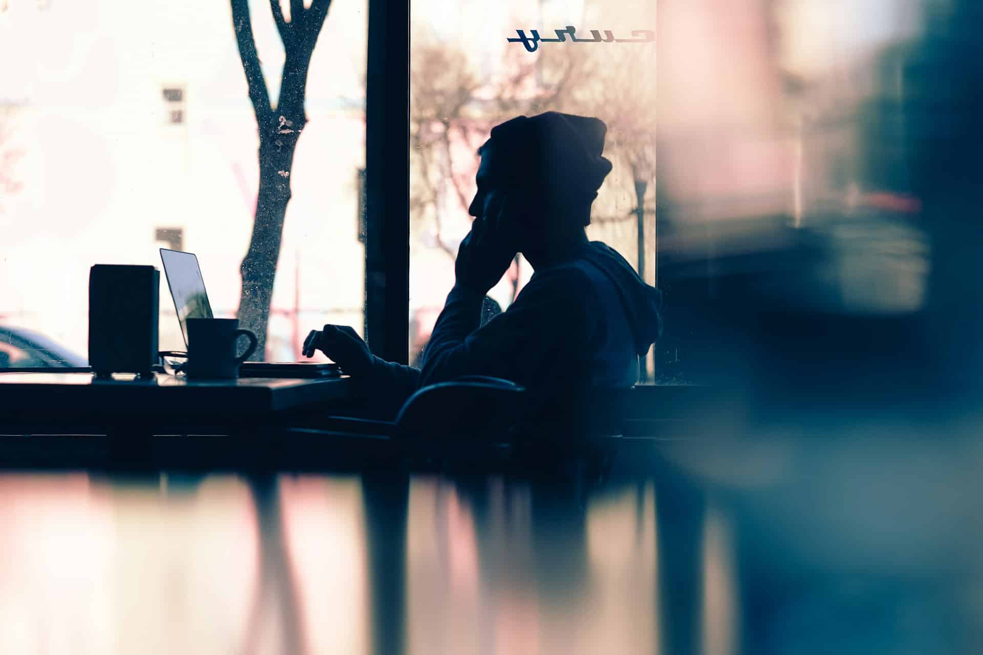 silhouette of person on phone with laptop