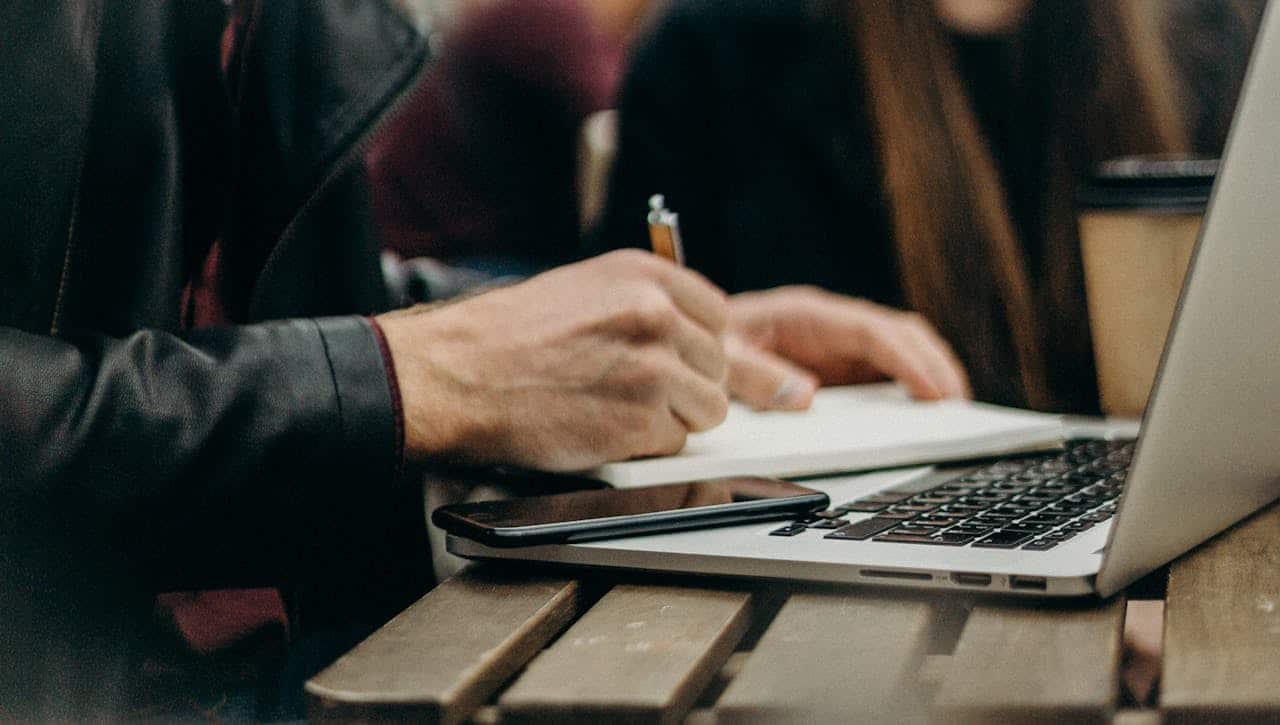 person taking notes with laptop open