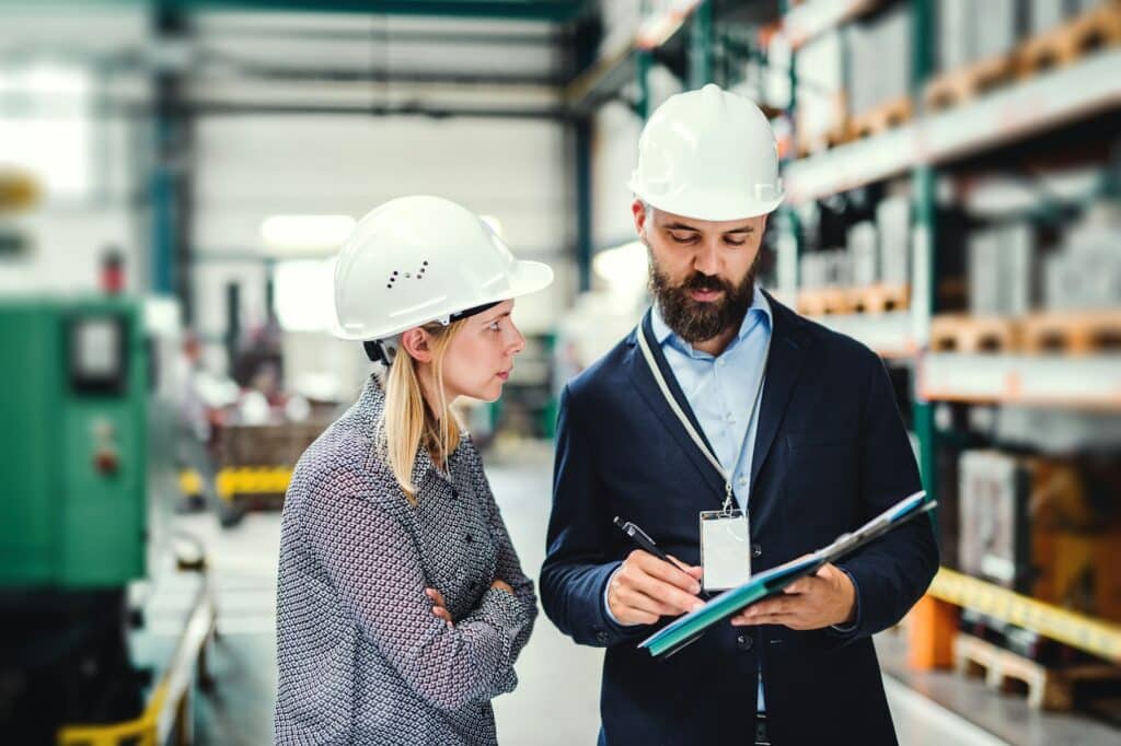 A senior construction worker providing feedback on a clipboard to an employee, representing employee discipline and performance management