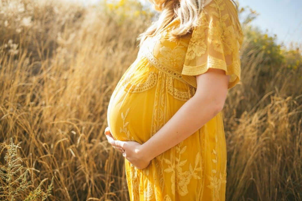 Pregnant woman in a yellow dress standing in a field, representing egg donors.