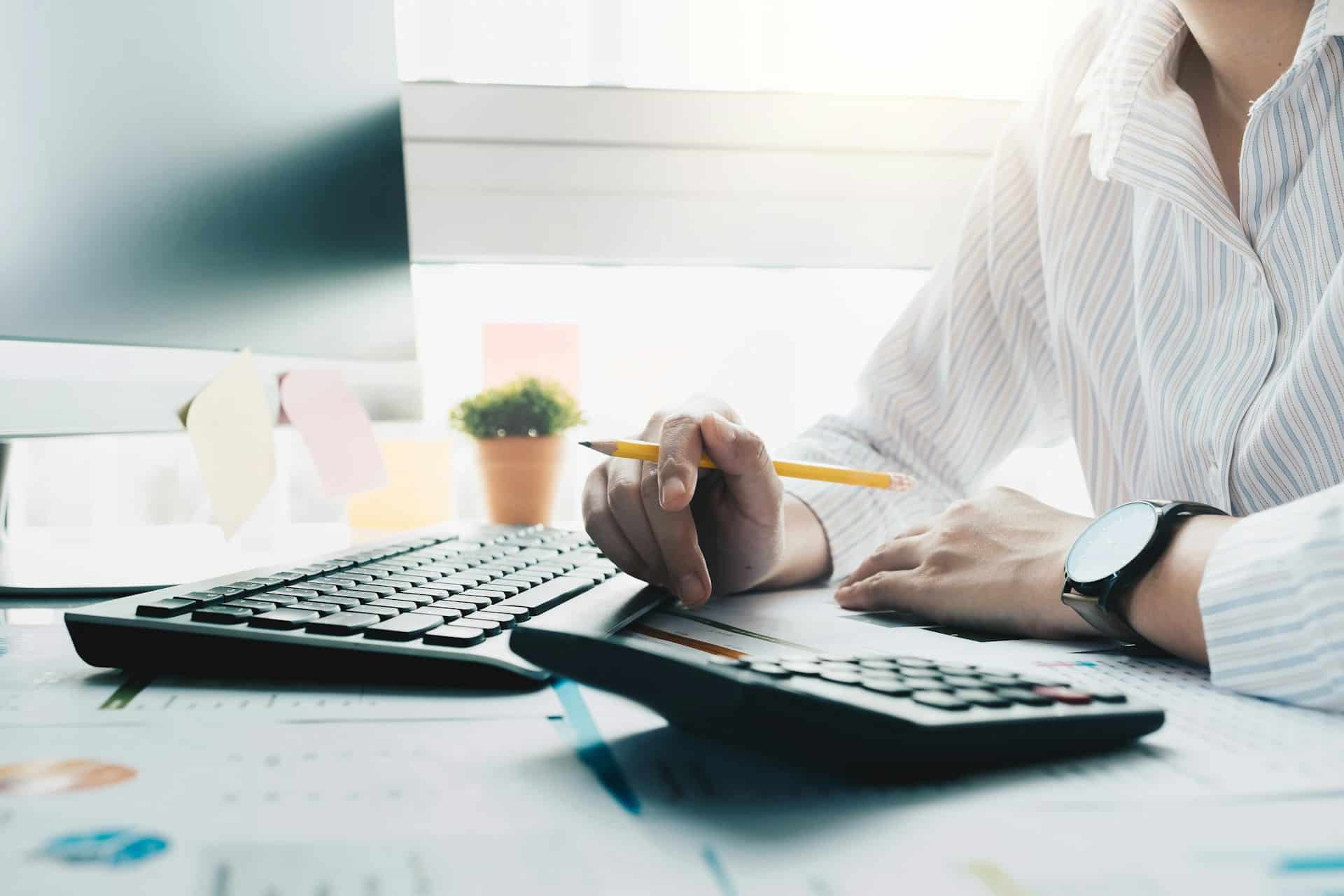 A woman at a desk with an adding machine and computer, representing unpaid invoices.
