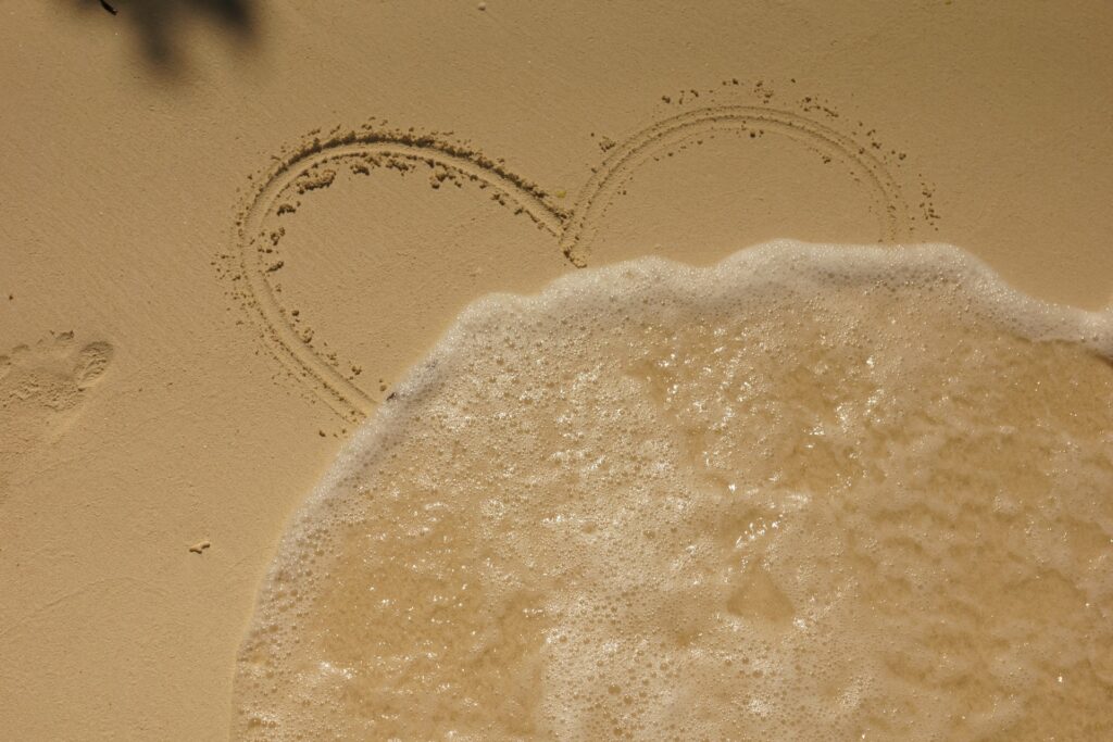 aerial photo of a heart drawn in the sand and water partially covering it