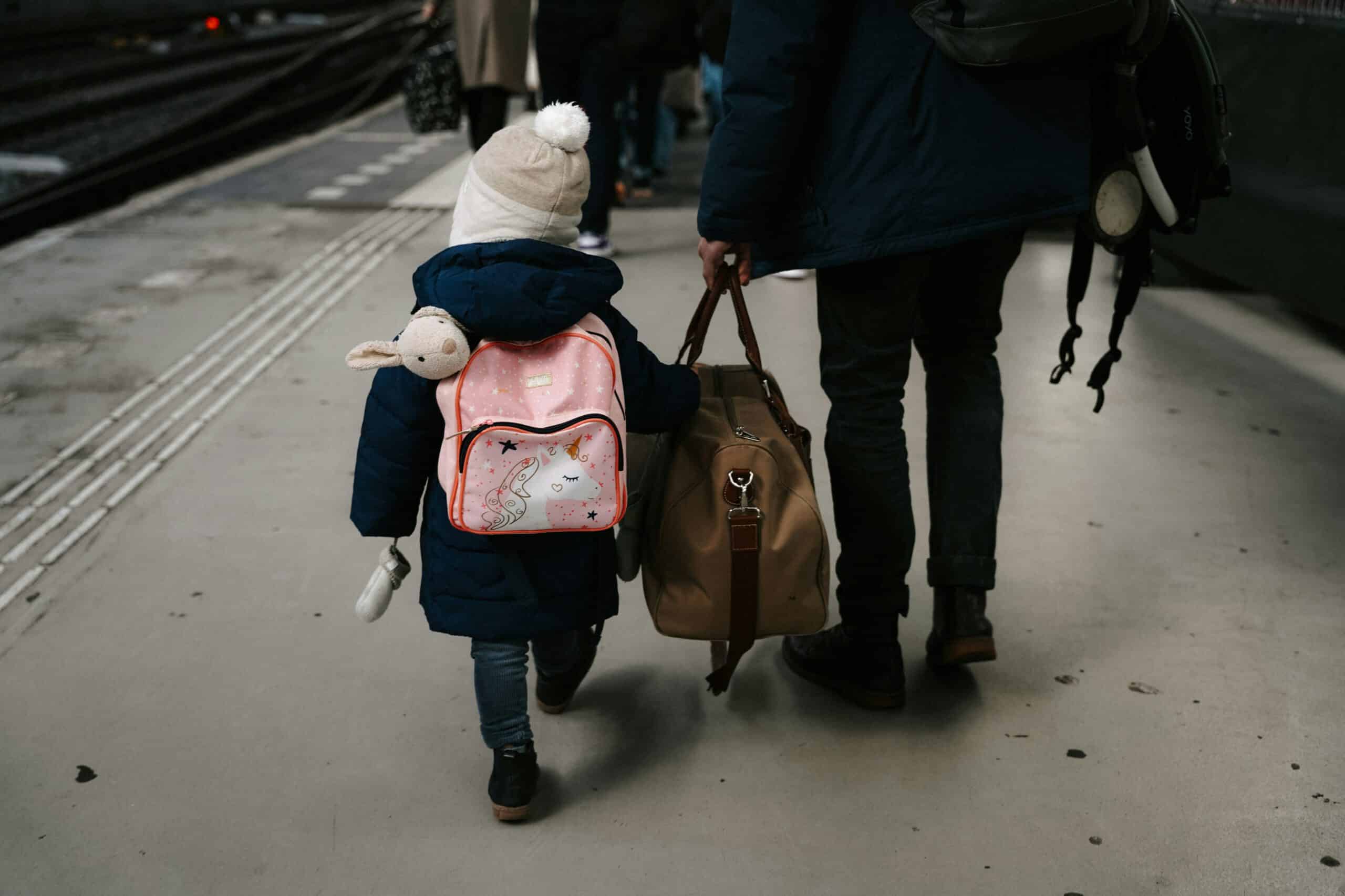 View from behind of an adult holding a bag, walking with a toddler with a pink backpack on, representing Child Support Law in Calgary and Strathmore, Alberta.