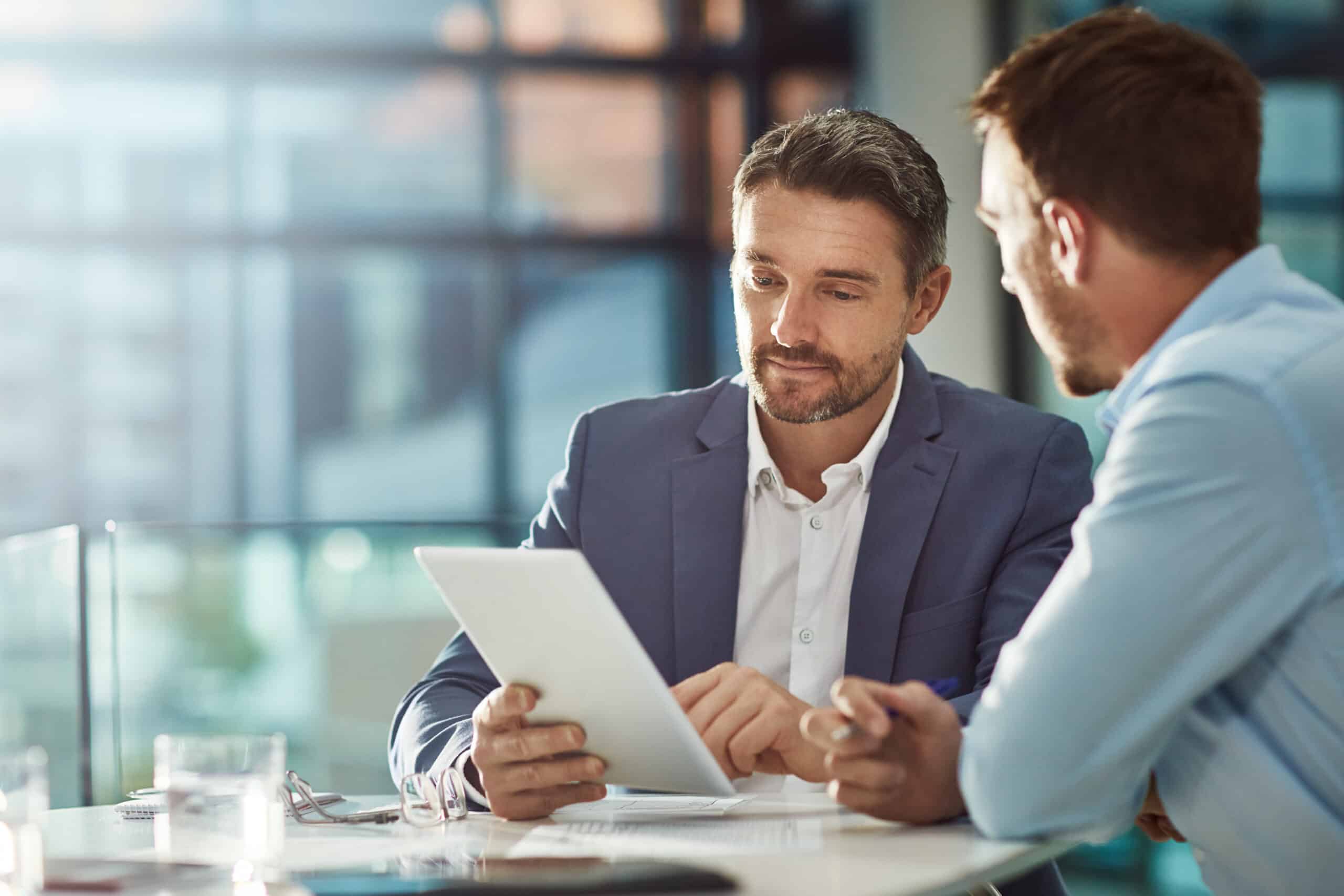 Two men working on a tablet together in a sunny office, representing Constructive Dismissal in Employment Law in Calgary, Alberta.