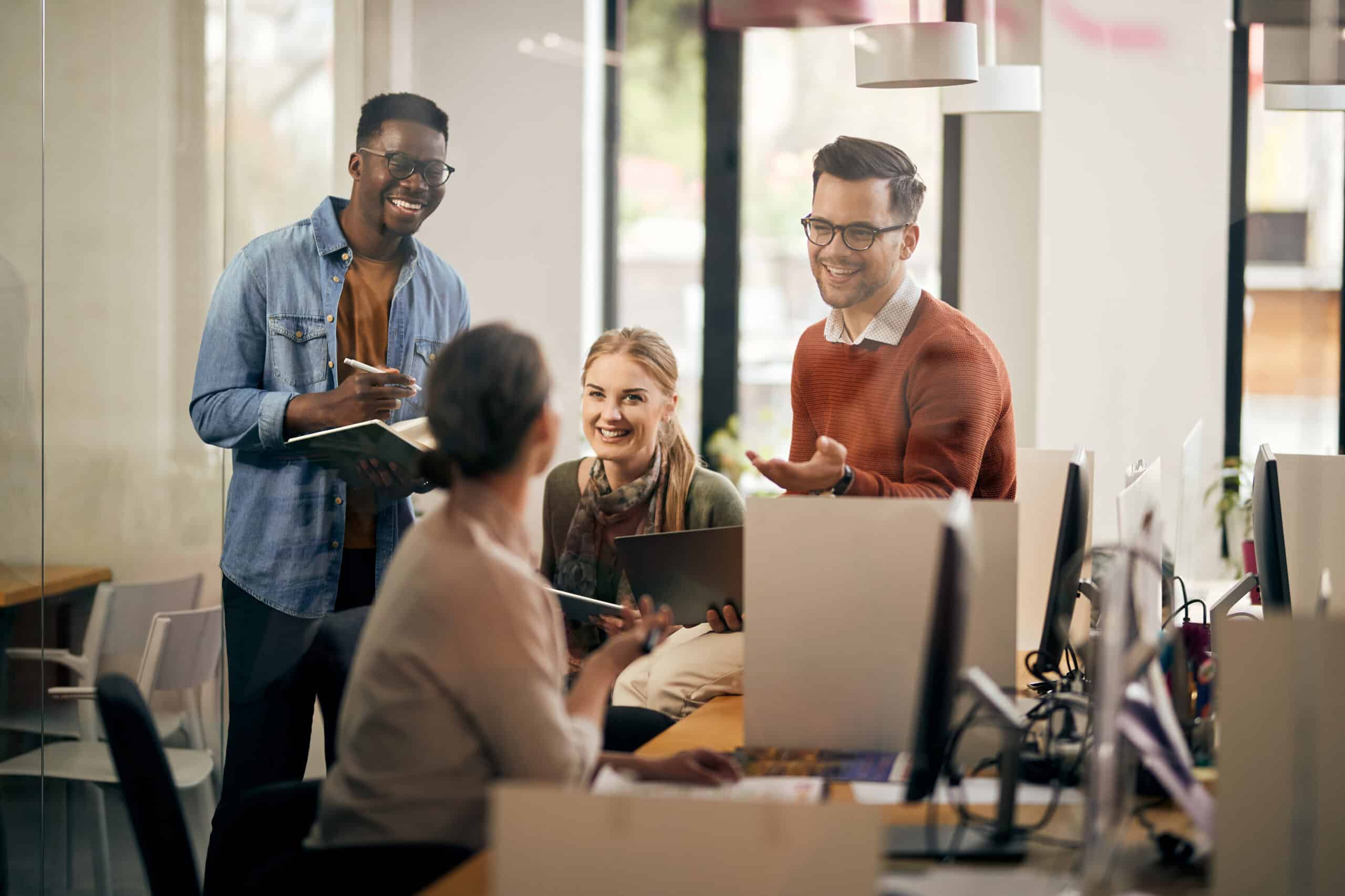 A group of colleages laughing and working together at a desk, representing inclusion, accommodation, and Human Rights in the Workplace in Calgary, Alberta.