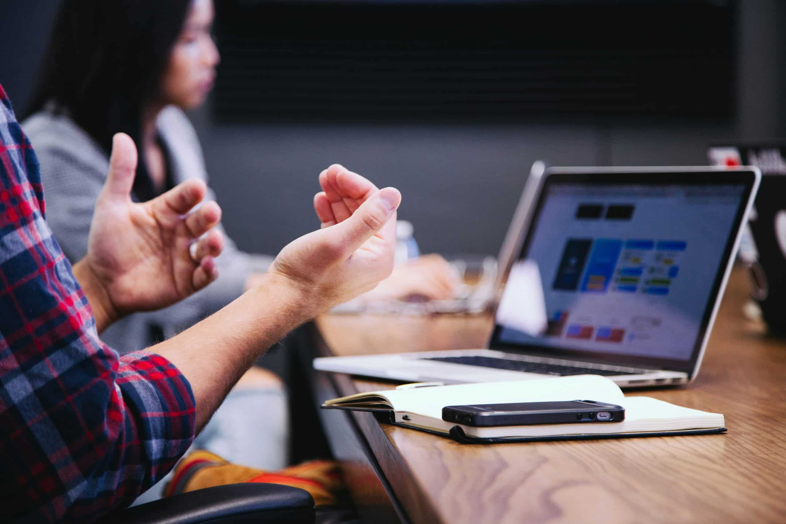 Close-up view of a person on their laptop with colleages around a boardroom table in the background, representing Performance Improvement Plans and Progressive Discipline in Calgary, Alberta employment law.
