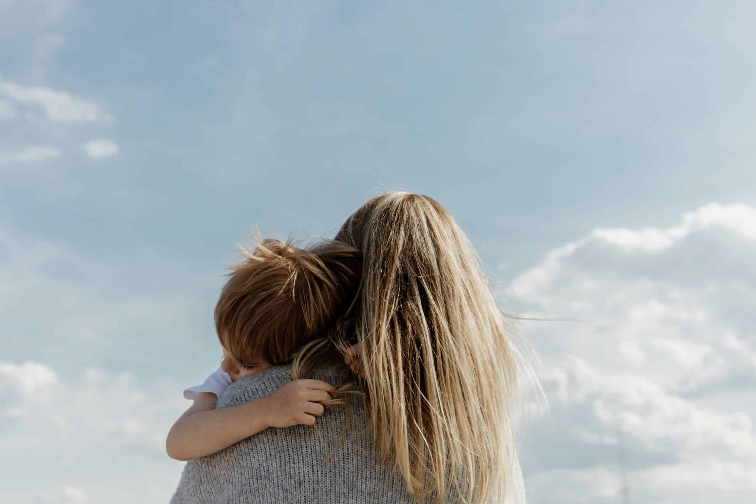 View from behind of a blonde woman holding a toddler who is resting on her shoulder, representing Spousal Support in Calgary and Strathmore, Alberta.