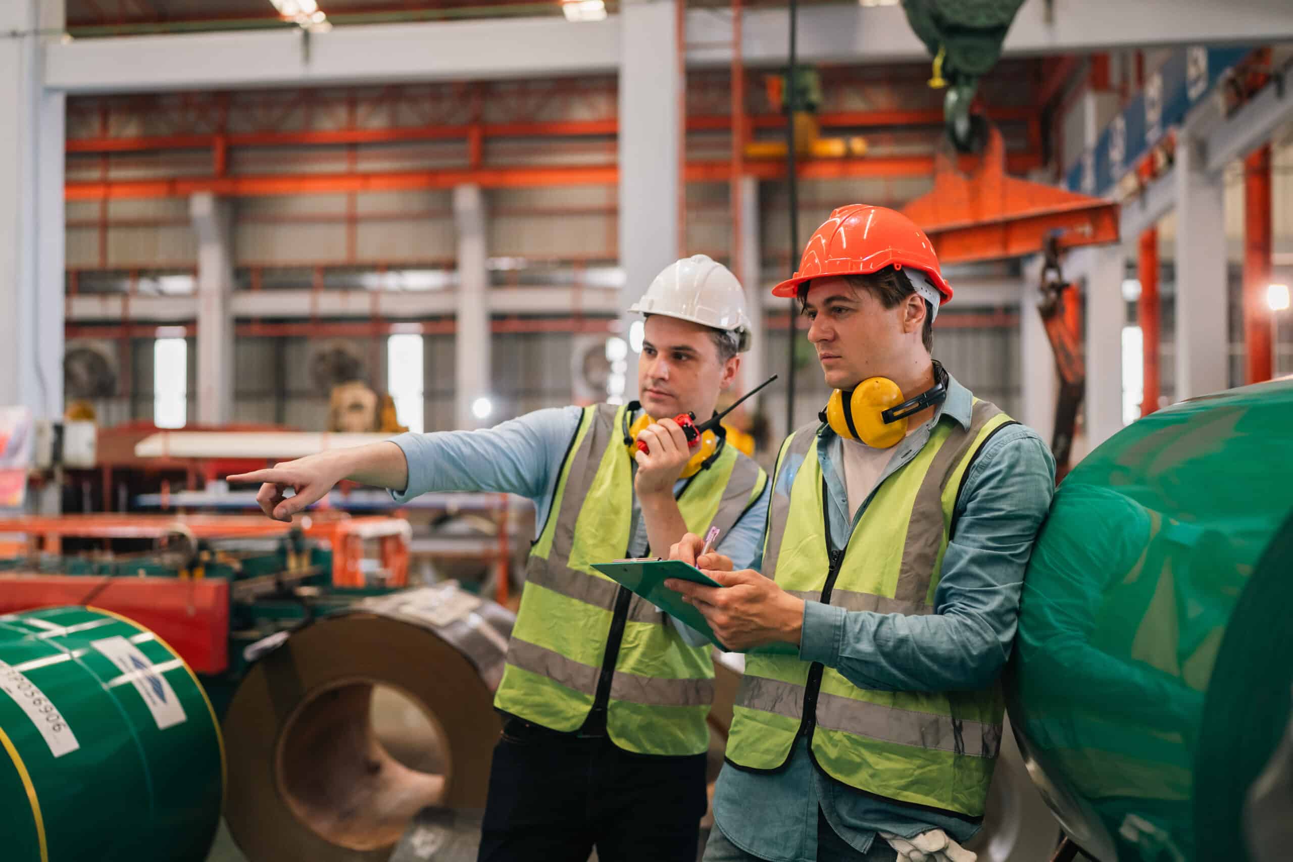 Two industrial workers in safety vests and hard hats in a factory site, representing Workplace Health and Safety in Calgary, Alberta.