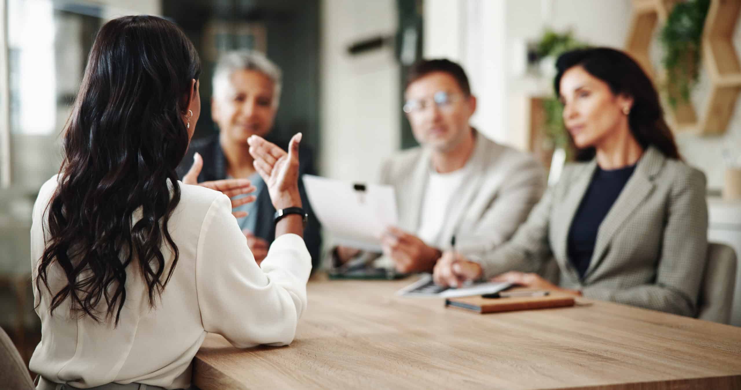 Colleages around a boardroom table with one person leading a discussion, representing Workplace Policies and Procedures in Calgary, Alberta.