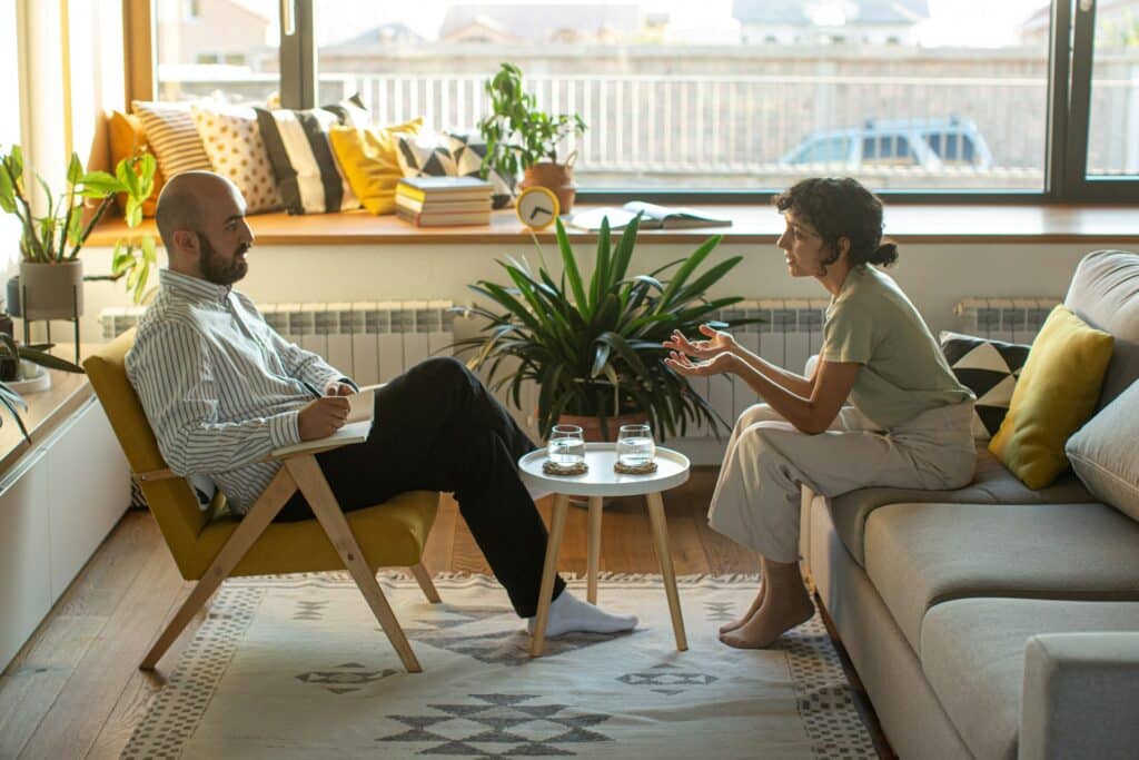Two people sitting across from each other in a sunlit therapist’s office, representing mental health and psychological safety in the workplace.