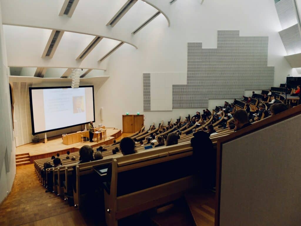 A professor teaches students in a lecture hall with a screen showing his lesson behind him, symbolizing an academic promotion dispute and workplace disability discrimination.