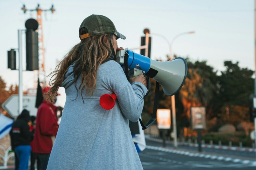 A woman shouts into a megaphone while standing at the side of blurred road alongside fellow strikers, representing replacement works in Alberta labour law.
